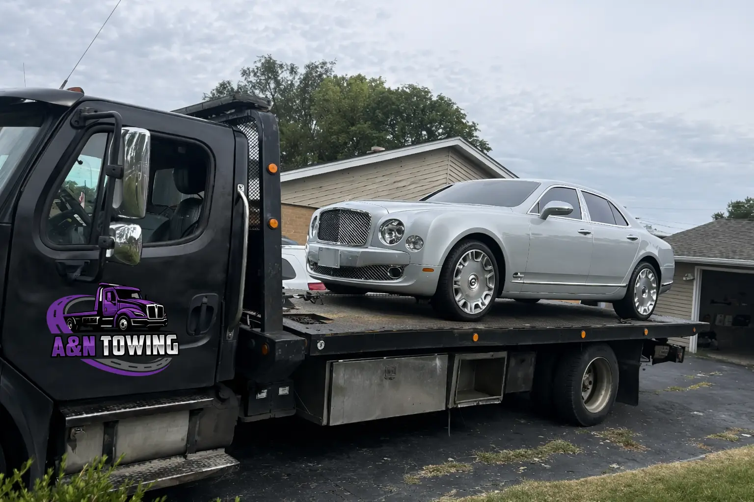 A&N Towing flatbed truck safely transporting a white Bentley Mulsanne luxury sedan in a Chicago suburb