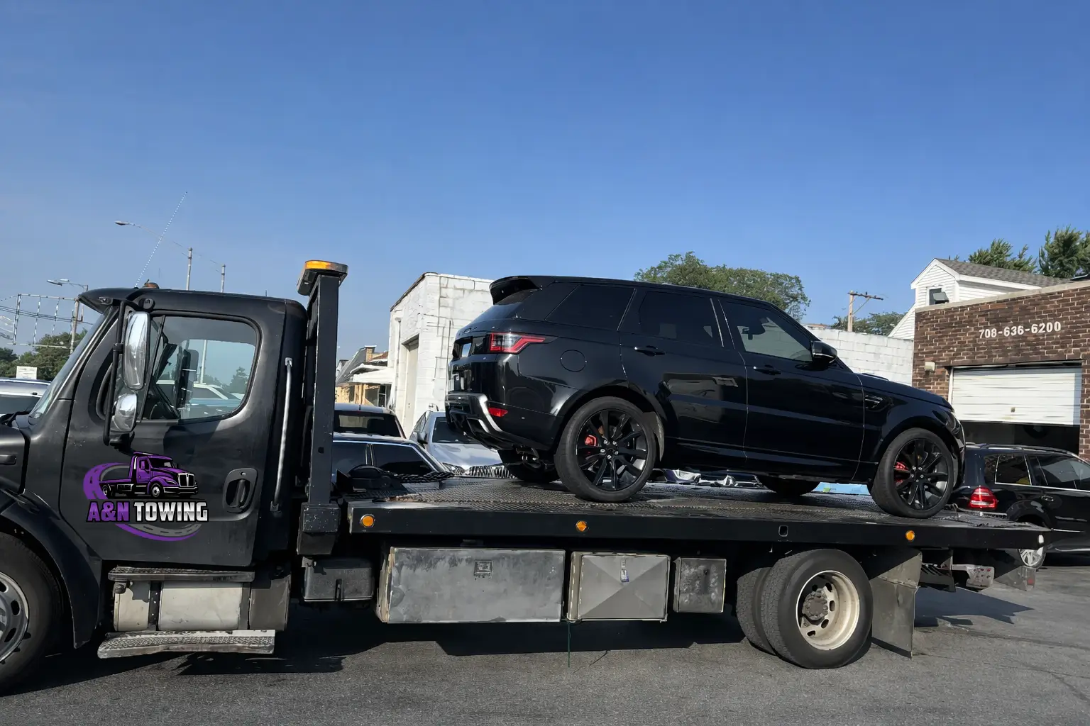 A&N Towing flatbed truck hauling a black Range Rover SUV through a suburban Chicago neighborhood