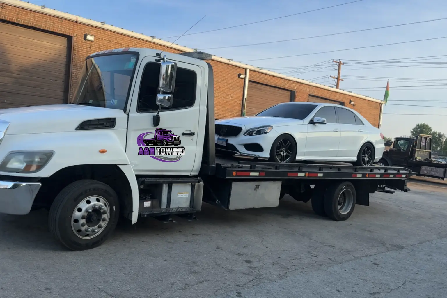 A&N Towing flatbed truck securely transporting a white Mercedes Benz sedan
