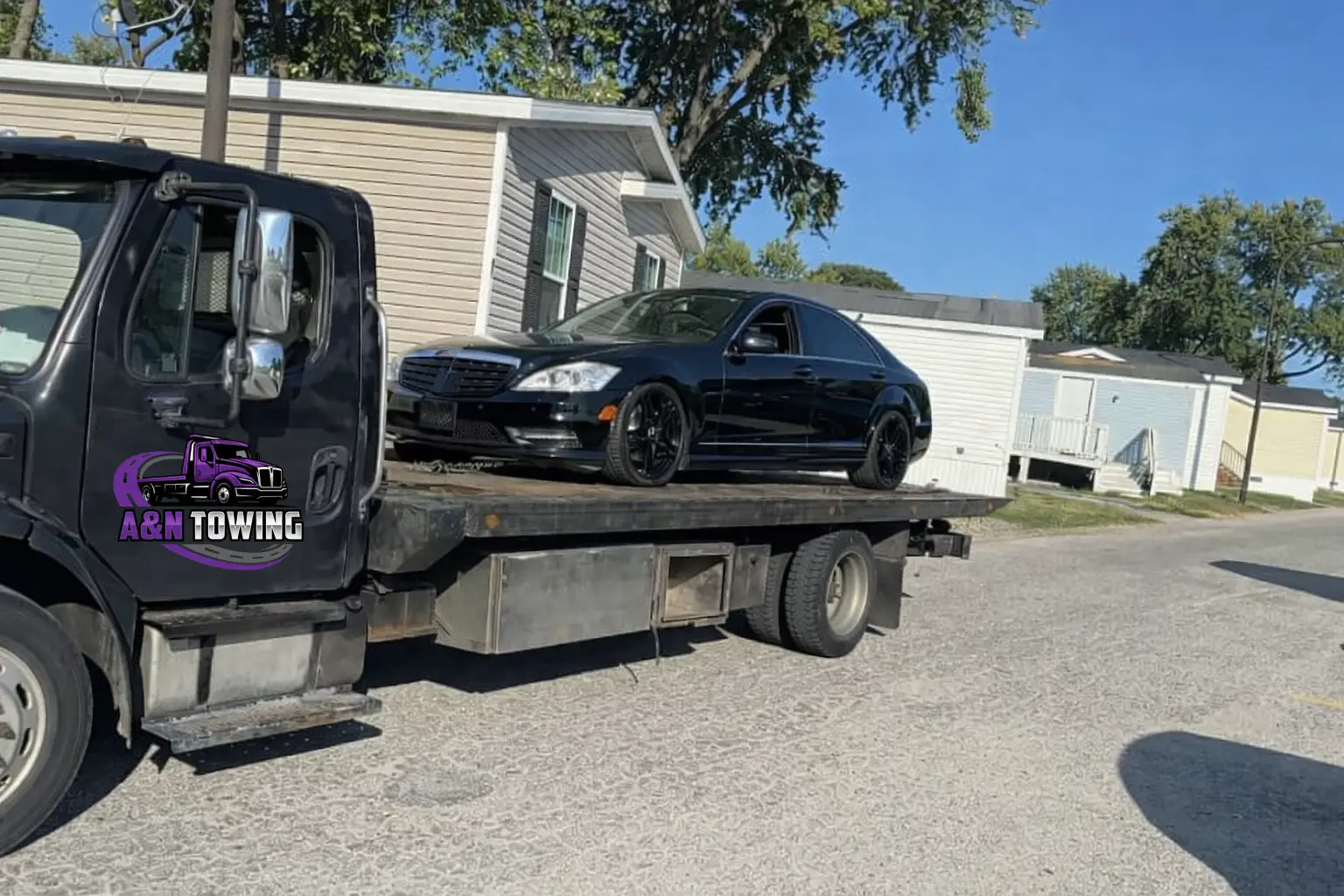 A&N Towing flatbed truck loading a black Mercedes sedan in a residential neighborhood for local vehicle transport