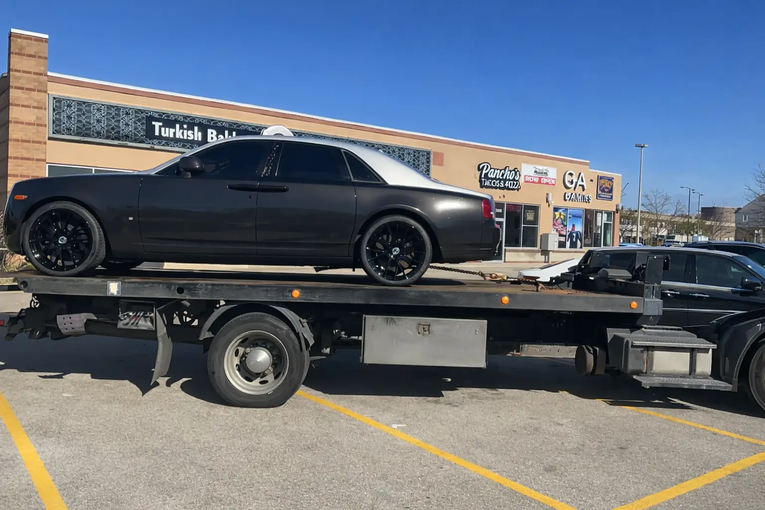 A&N Towing flatbed truck loading a black Rolls Royce in a Chicago parking lot for safe luxury vehicle transport